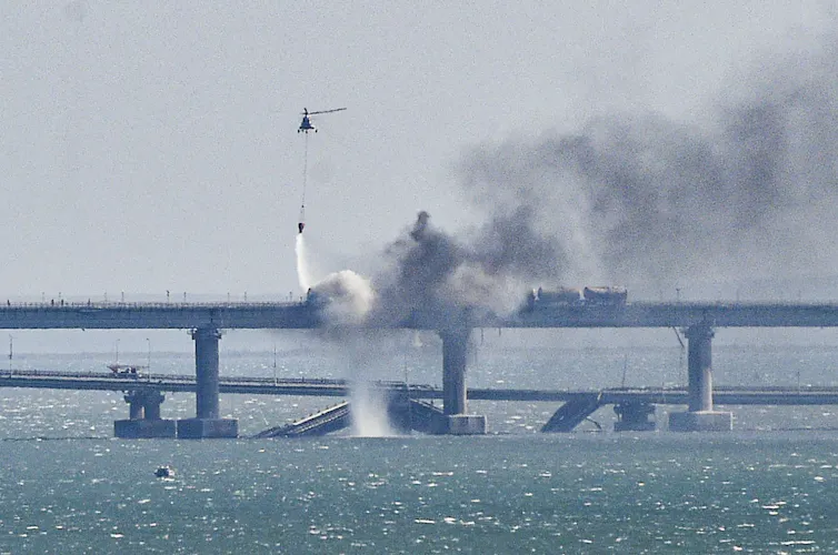 A helicopter pours water on a fire on a collapsed part of a bridge.