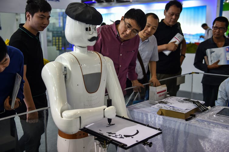 A robot paints as people watch.