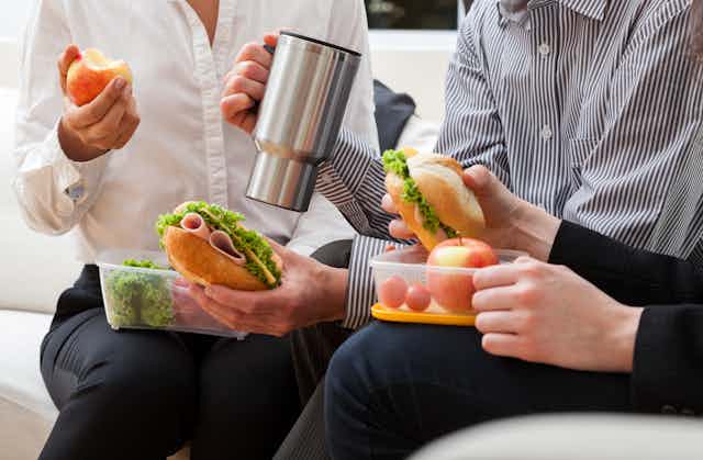 Photo of three colleagues eating sandwiches out of tupperware, sitting side by side