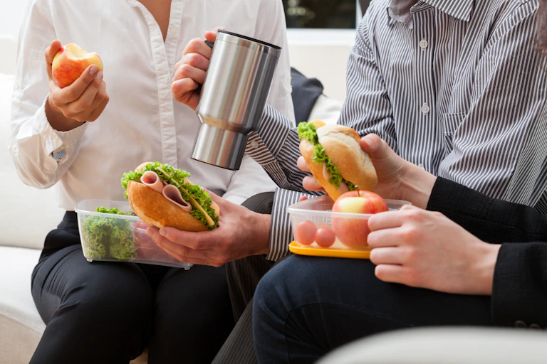 Photo of three colleagues eating sandwiches out of tupperware, sitting side by side