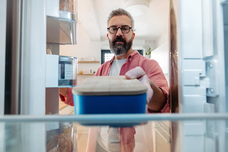 A man places a sealed container of food in the fridge.