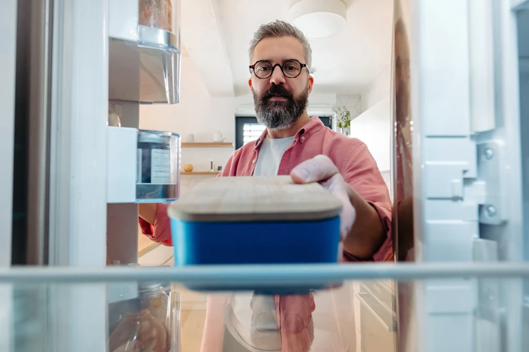 A man places a sealed container of food in the fridge.