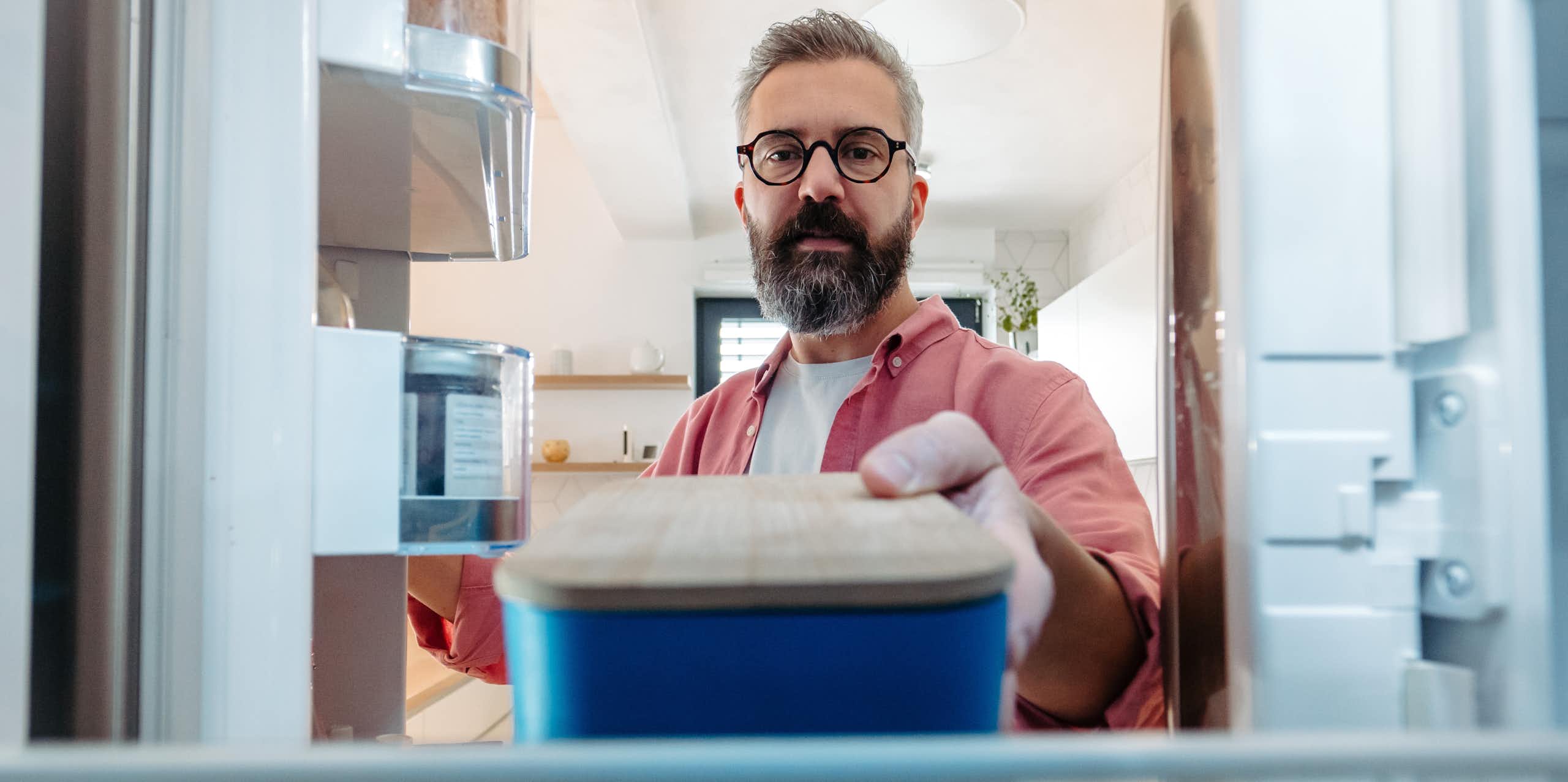 A man places a sealed container of food in the fridge.