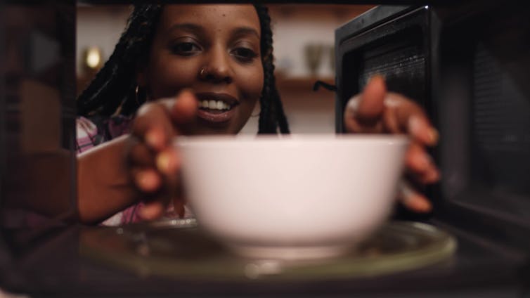 A woman places a bowl in the microwave to reheat.