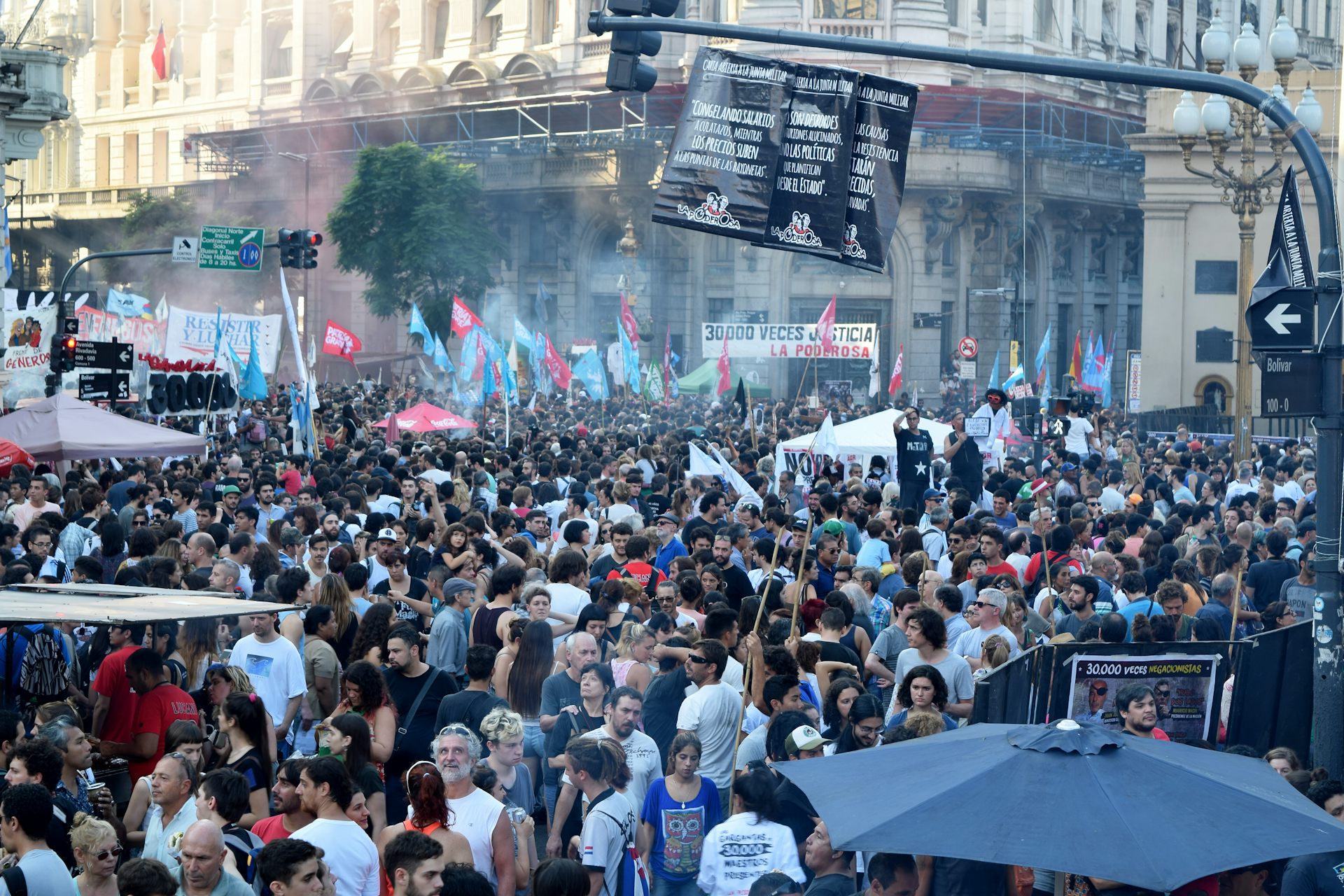 A large crowd of people in a street holding banners and pictures aloft.