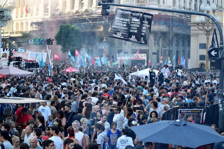 A large crowd of people in a street holding banners and pictures aloft.