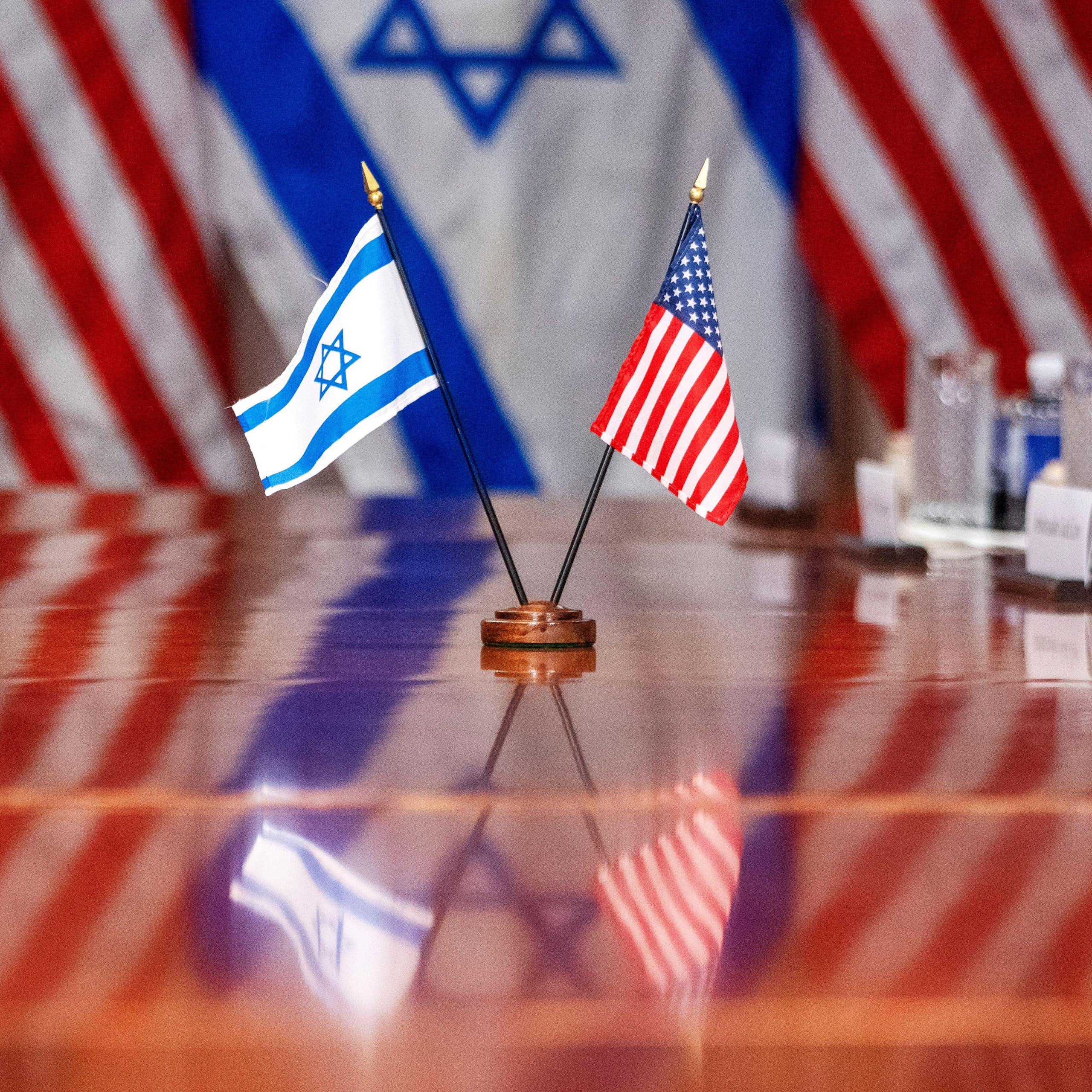 Israeli and US flags together on a polished boardroom table.