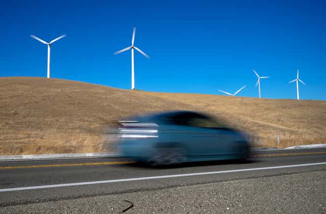 A blurred vehicle races past wind turbines.