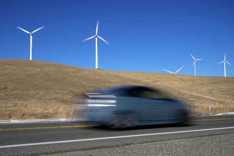 A blurred vehicle races past wind turbines.