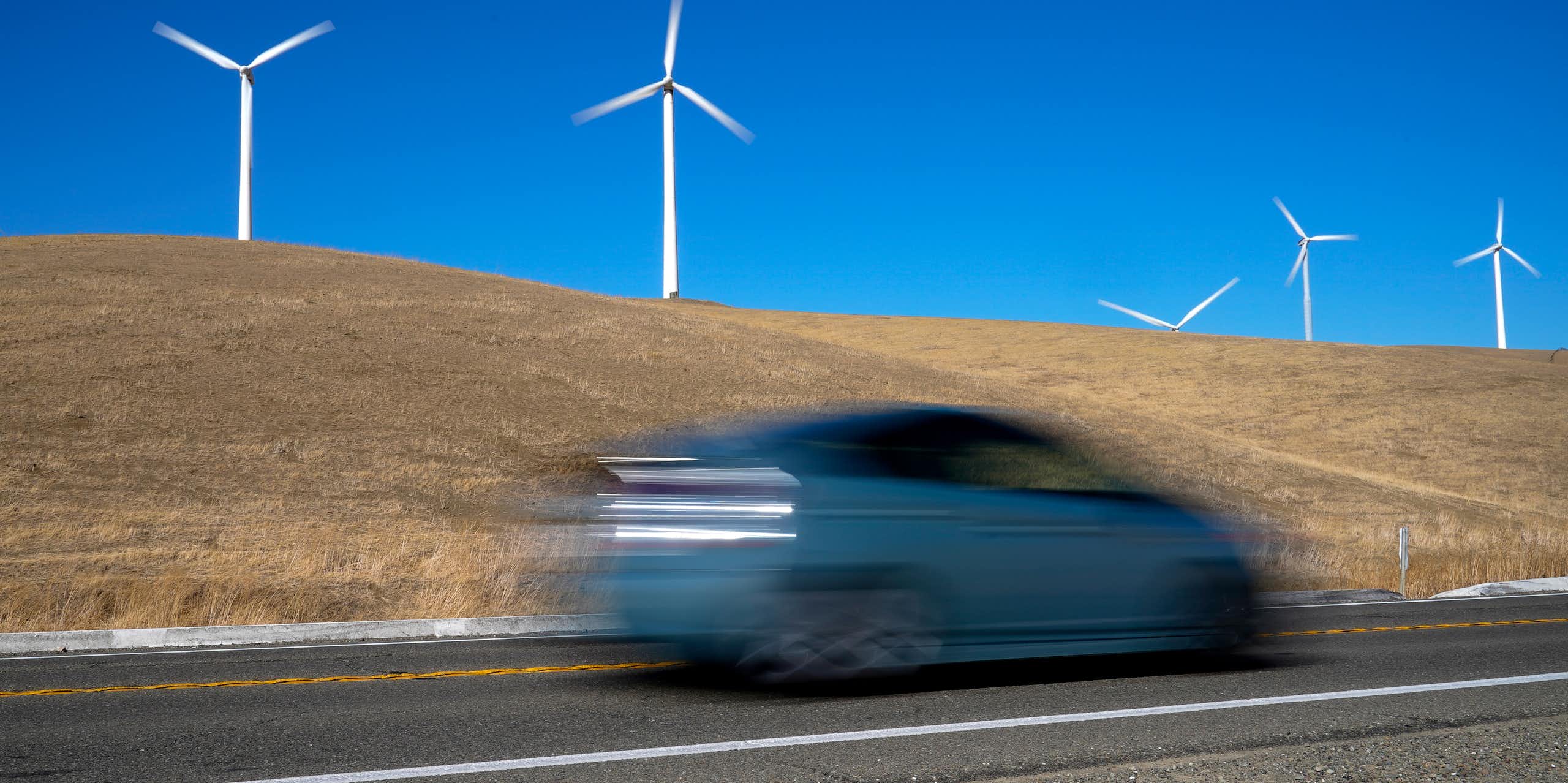 A blurred vehicle races past wind turbines.