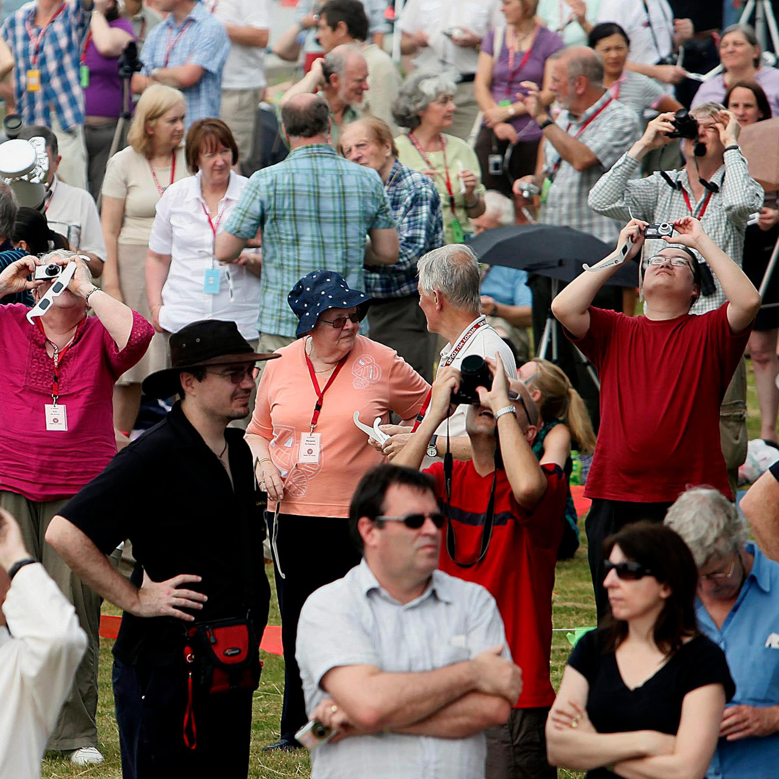 Des personnes debout regardent le ciel en portant des lunettes d'éclipse, tandis que des personnes dans la foule tiennent des appareils photo.