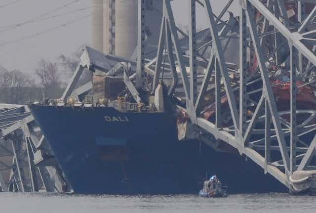 the front of a container ship floats with large chunks of the bridge it crashed into lying on top