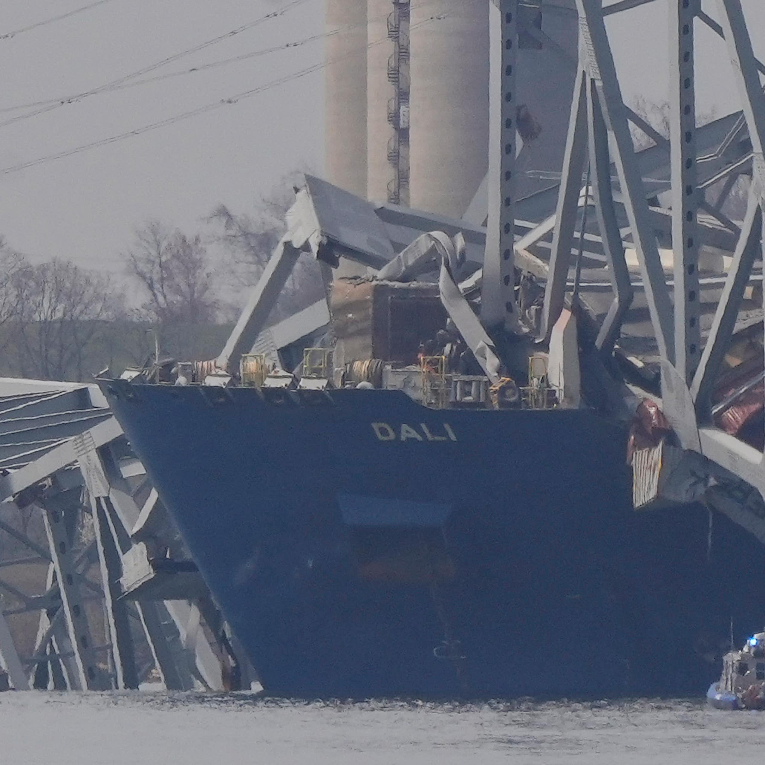 the front of a container ship floats with large chunks of the bridge it crashed into lying on top
