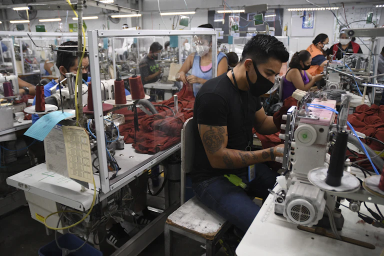 Workers in face masks sit next to sewing machines.