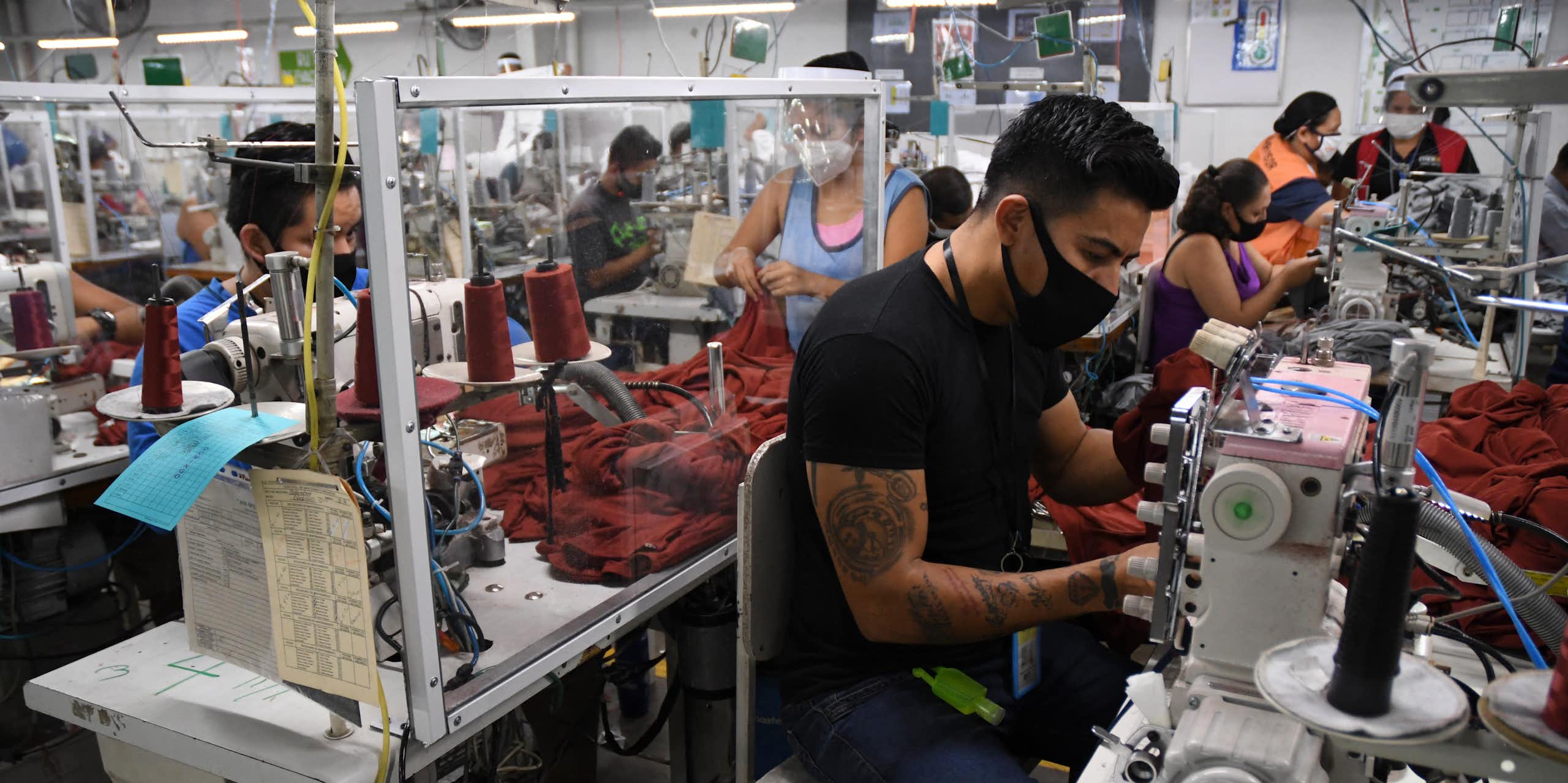 Workers in face masks sit next to sewing machines.