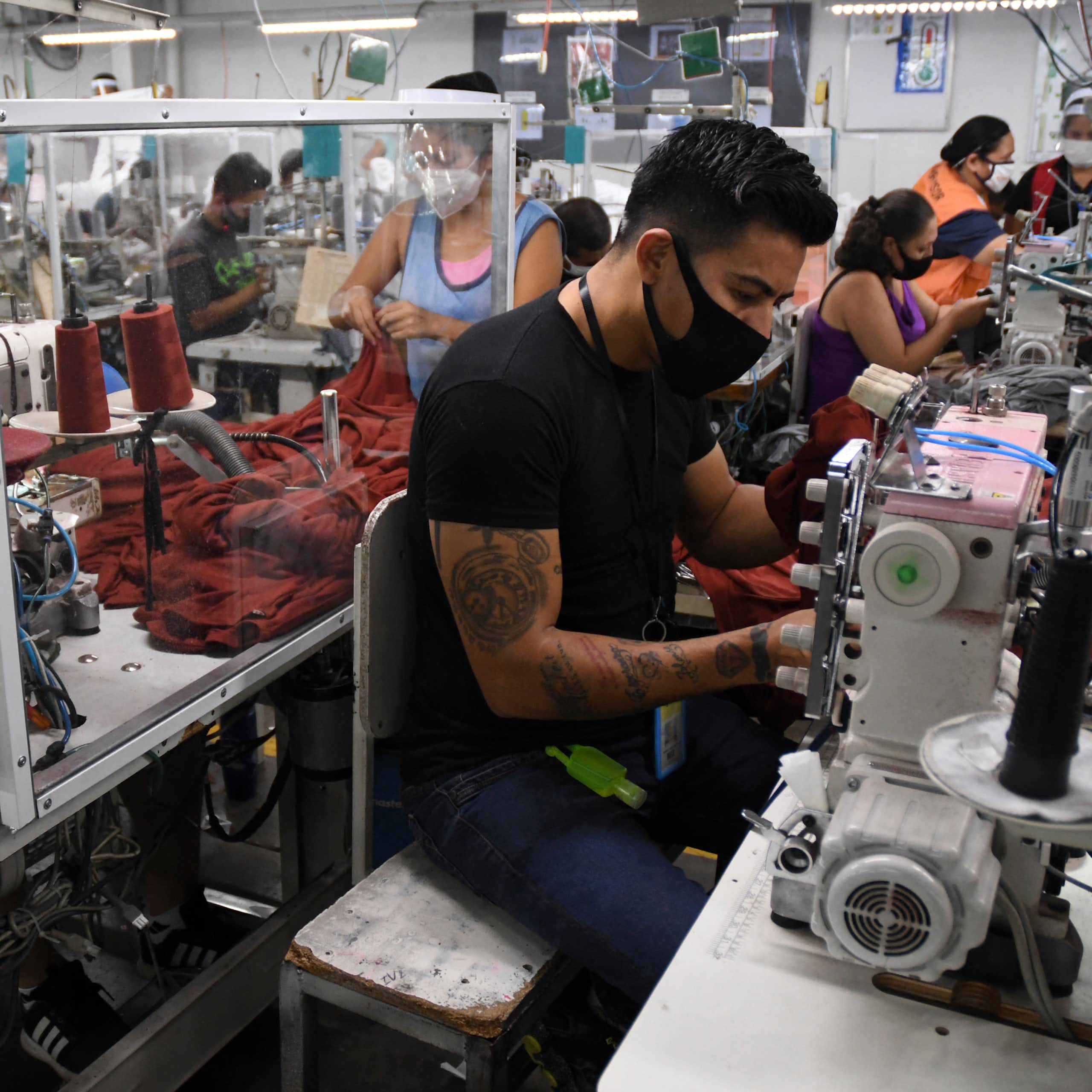 Workers in face masks sit next to sewing machines.