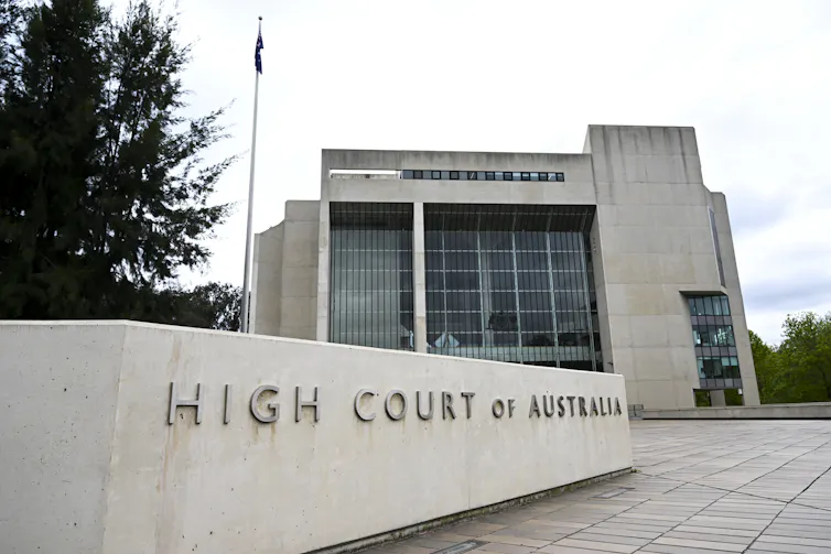 The exterior of a tall concrete building and a concrete sign that reads 'High Court of Australia'.