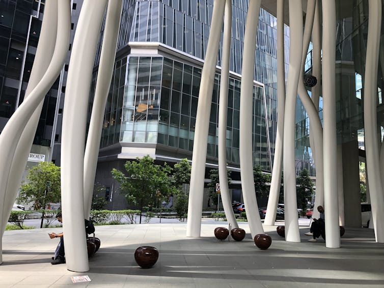 Wavy columns outside a building. Square windows can be seen on neighbouring building