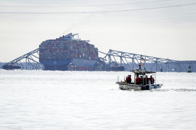 Photo shows US Coast Guard boat sailing towards a container ship entangled in the wreckage of a large bridge.