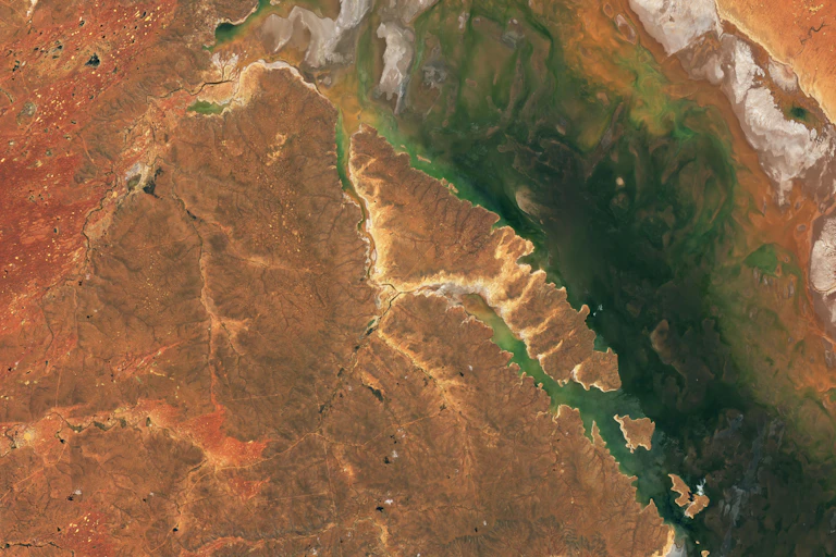 An aerial view of red soil and a dark teal lake.