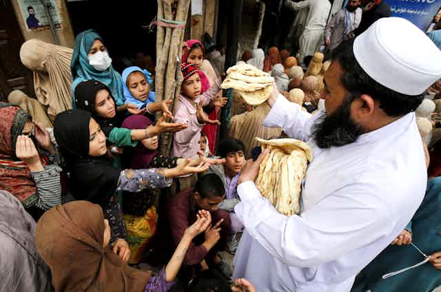 A man hands out flatbread to a crowd of Muslim women and children