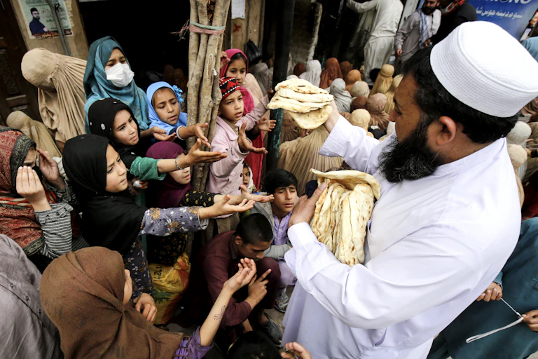 A man hands out flatbread to a crowd of Muslim women and children
