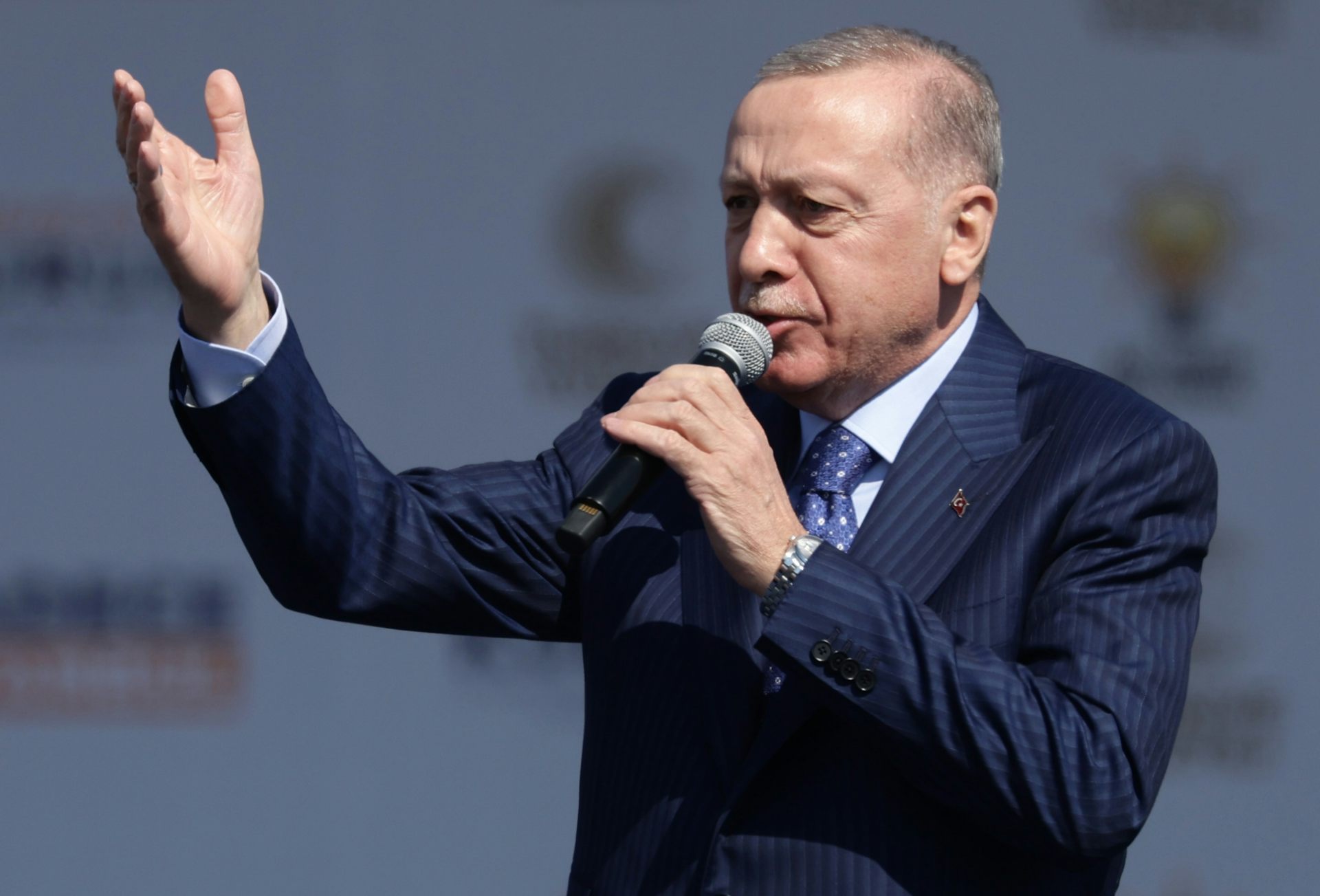 Recep Tayyip Erdoğan speaking into a microphone with his right arm outstretched.