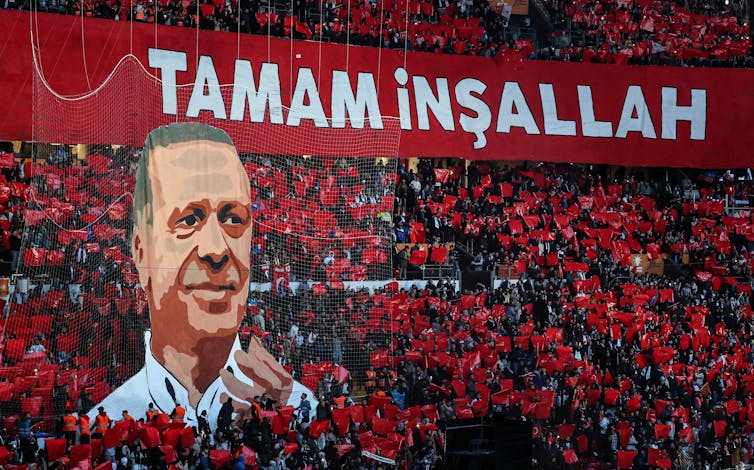 A stand full of people holding red placards and a large picture depicting Turkish president, Recep Tayyip Erdoğan.