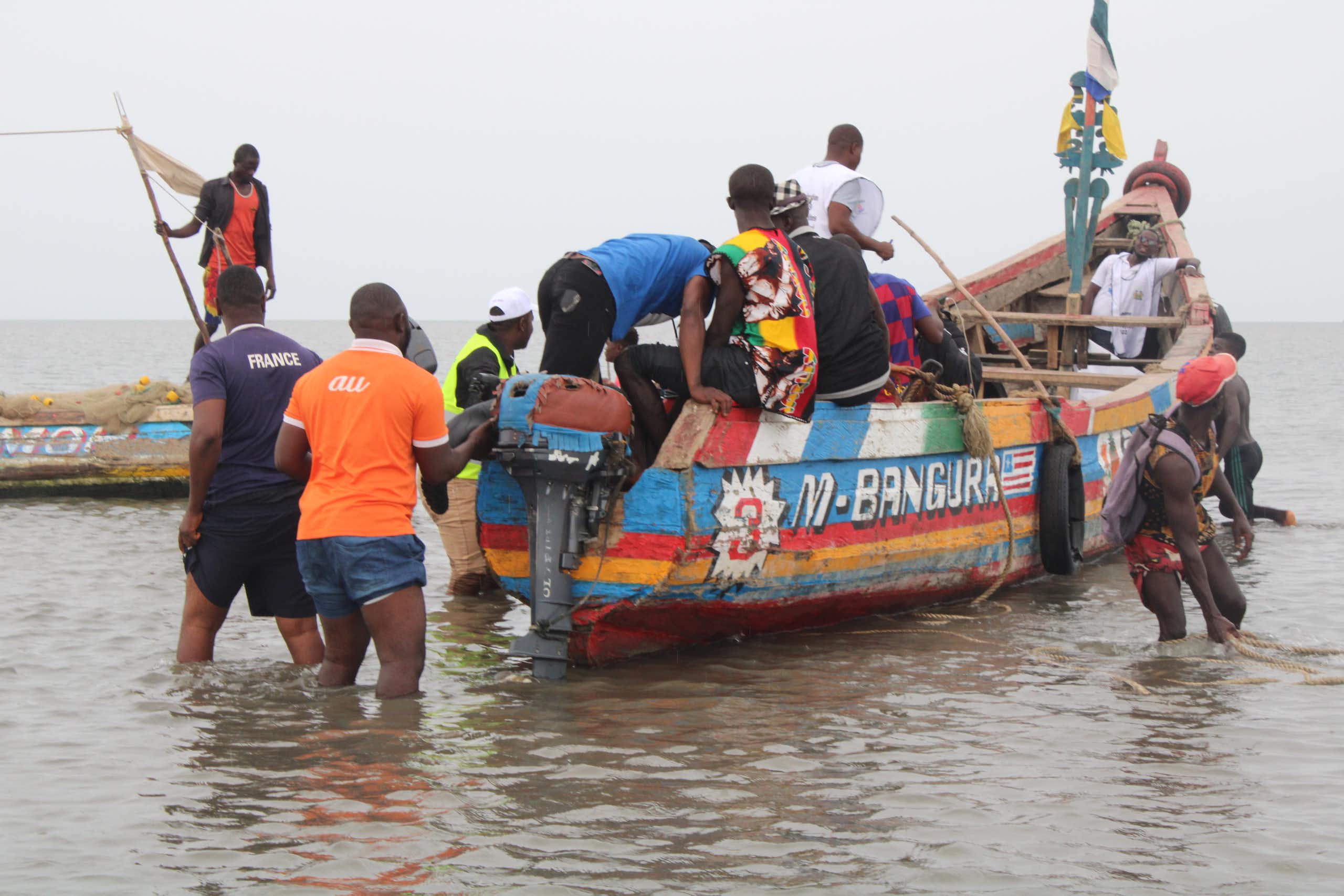 A colourfully painted small boat in shallow water with people standing around and in it.