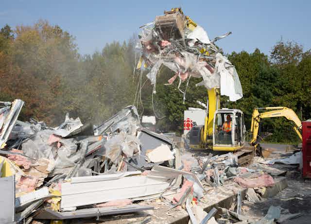 A man in a bulldozer tears down a structure.