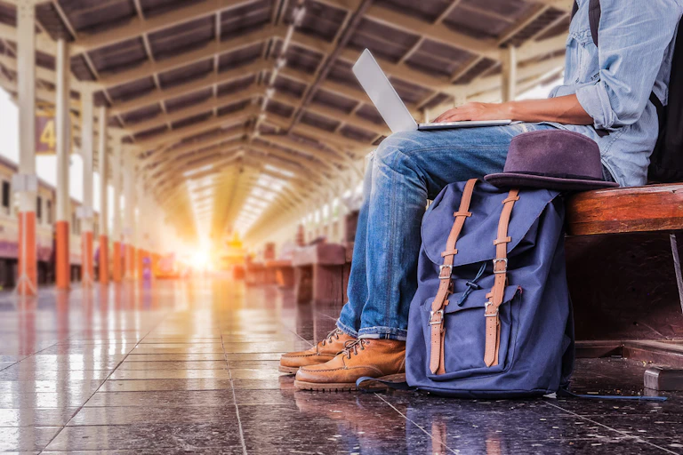 Homme assis avec un sac à dos et un ordinateur dans une gare