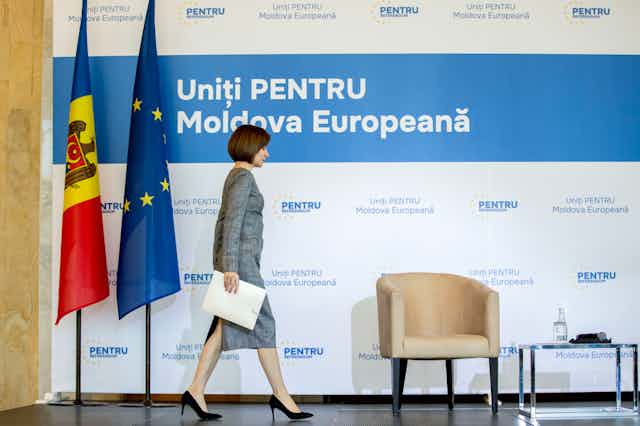 Moldovan president Maia Sandu.walks across a stage in front of Moldovan and EU flags.