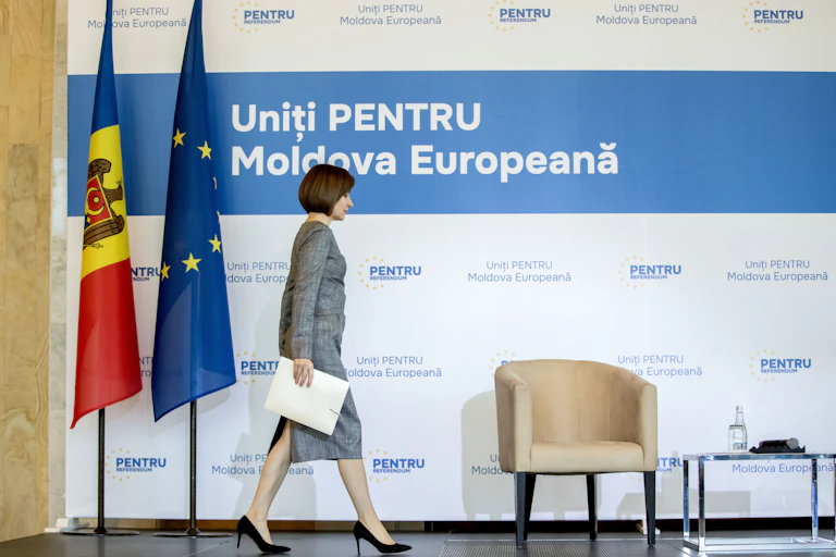 Moldovan president Maia Sandu.walks across a stage in front of Moldovan and EU flags.
