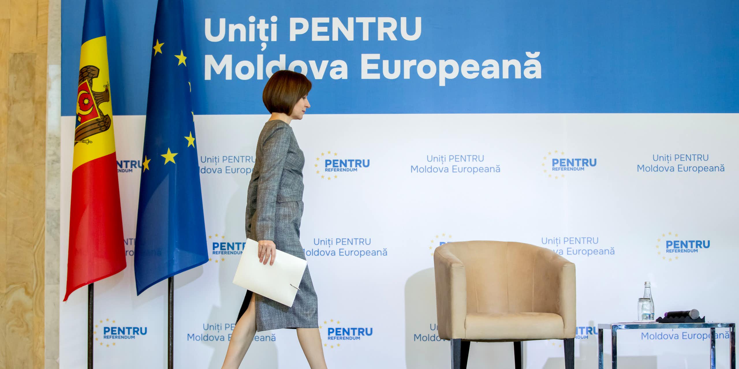 Moldovan president Maia Sandu.walks across a stage in front of Moldovan and EU flags.