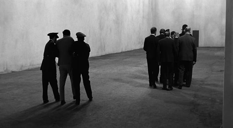 A group of people accompanies a man while two men drag another one behind them.