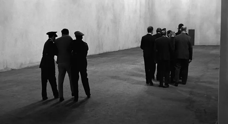 A group of people accompanies a man while two men drag another one behind them.