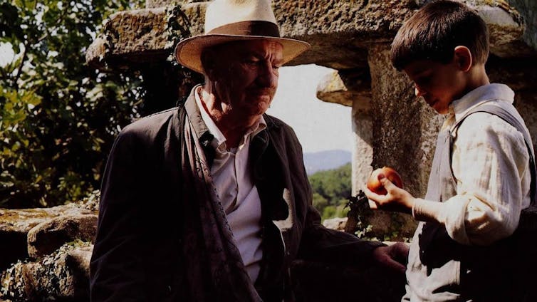 An old man and a boy talk in a forest.