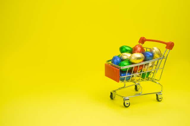 A small toy shopping trolley containing chocolate eggs wrapped in colourful foil.