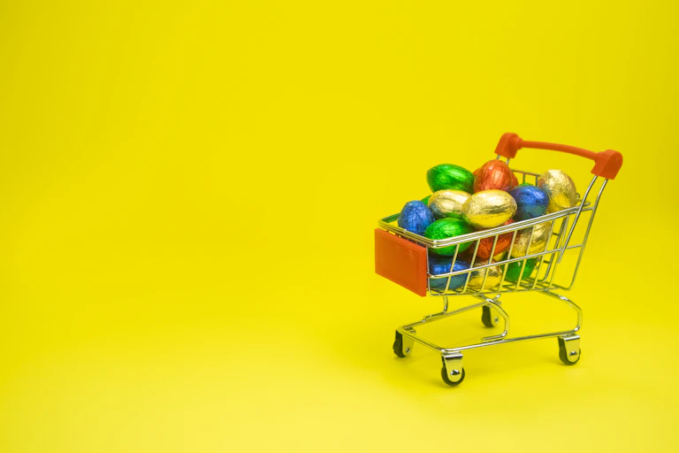 A small toy shopping trolley containing chocolate eggs wrapped in colourful foil.