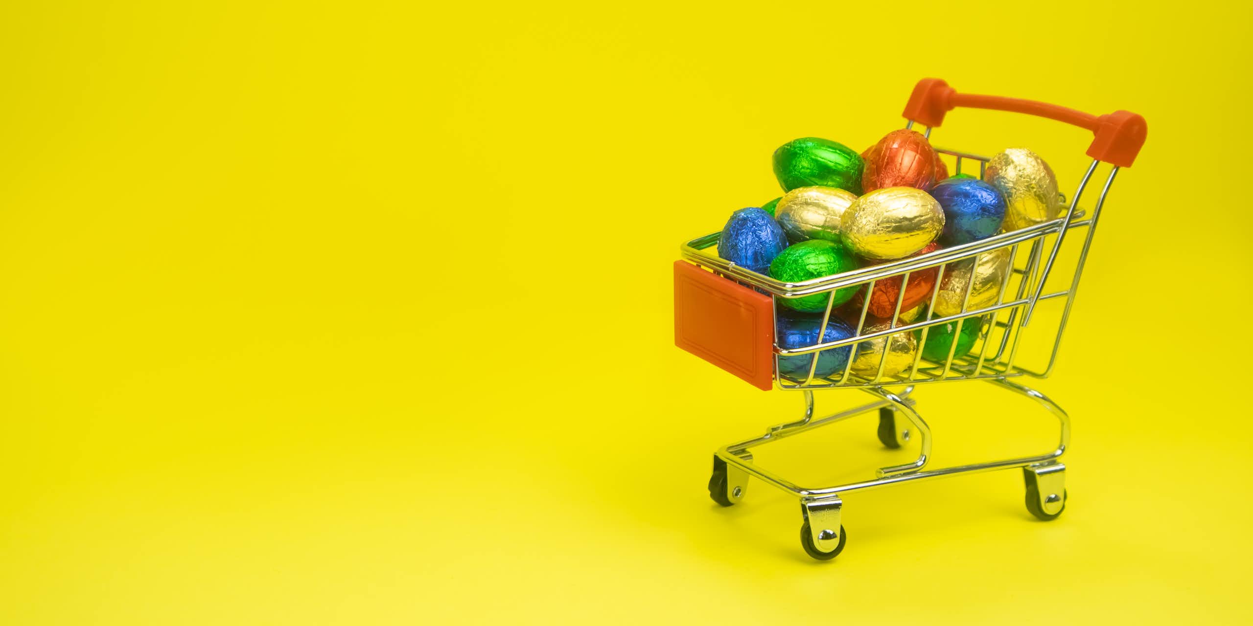 A small toy shopping trolley containing chocolate eggs wrapped in colourful foil.