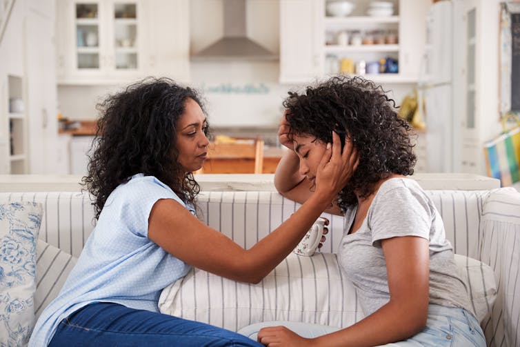 A mother comforts a distraught teenager on a sofa.