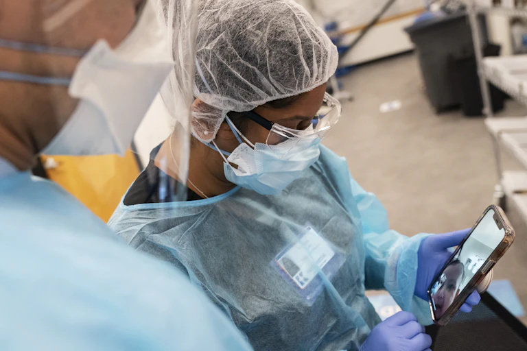Two people wearing personal protective equipment look at a smartphone.