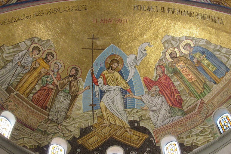 Um mosaico com fundo dourado, seis figuras com halos, Jesus segurando uma cruz no meio e duas pessoas que ele está ajudando a sair de caixões.