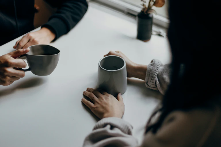 cropped image of two people's hands holding mugs across from each other at a table