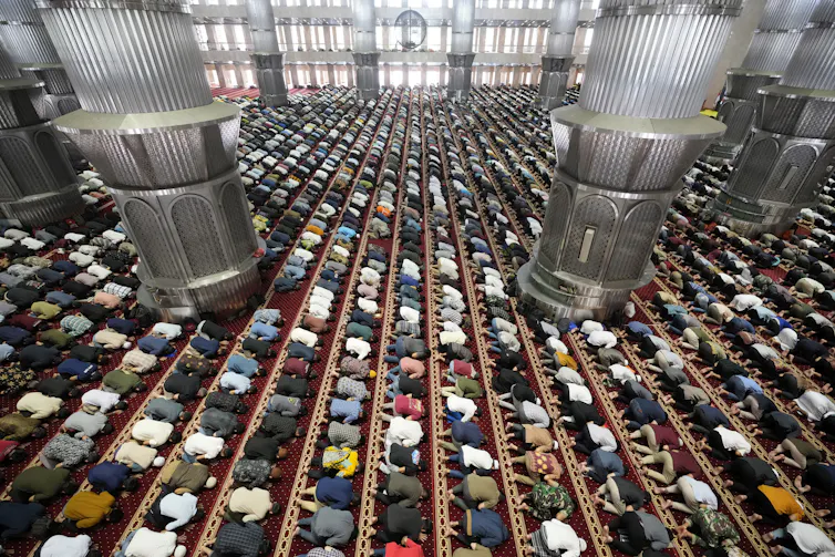 An aerial view of hundreds of Muslims kneeling in prayer in a large Mosque