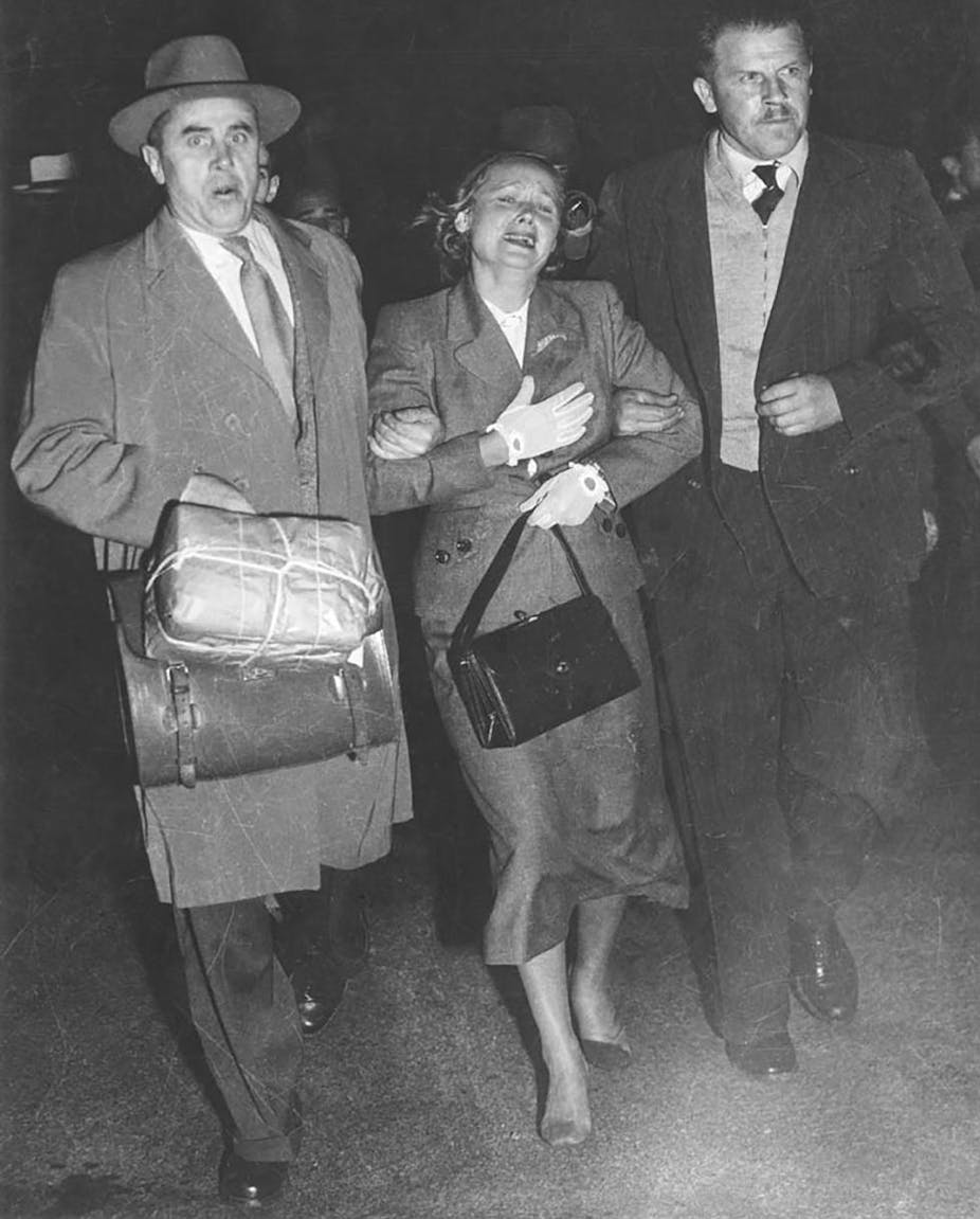 Royal Commission on Espionage - Exhibit 62: Large black and white photograph of Evdokia Petrov at Mascot Airport, Sydney, being 'escorted' across the tarmac to a waiting plane by two armed Russian diplomatic couriers.