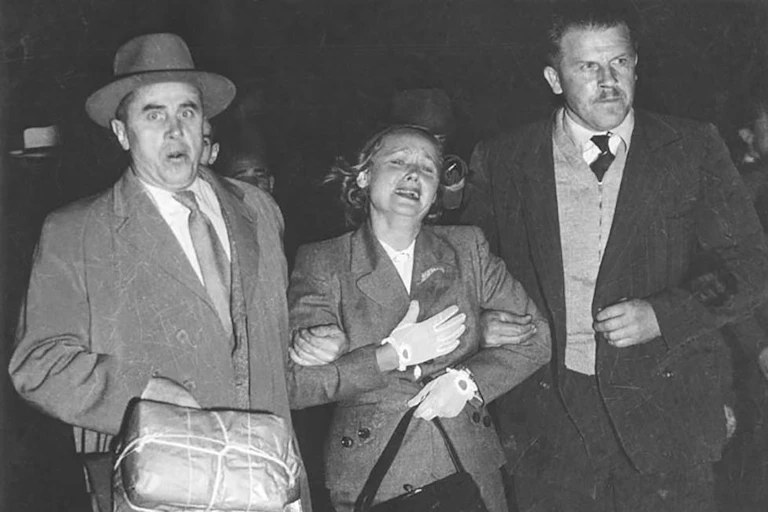 Royal Commission on Espionage - Exhibit 62: Large black and white photograph of Evdokia Petrov at Mascot Airport, Sydney, being 'escorted' across the tarmac to a waiting plane by two armed Russian diplomatic couriers.