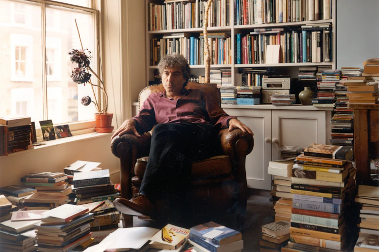 Adam Phillips sits in an armchair in his book-filled office.