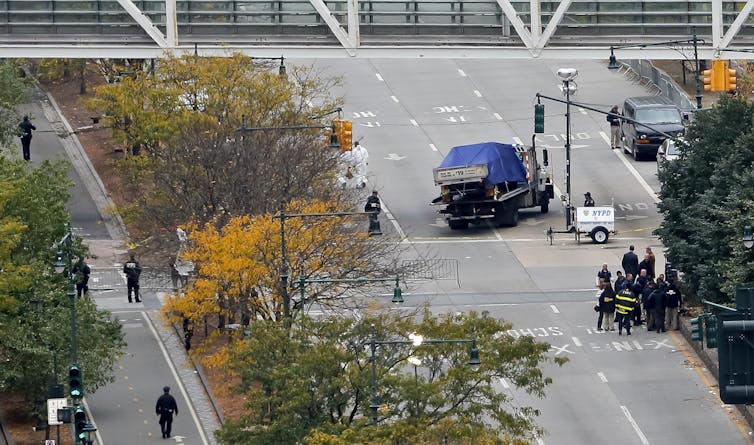 The wreckage of a truck under a blue sheet is seen being towed away.