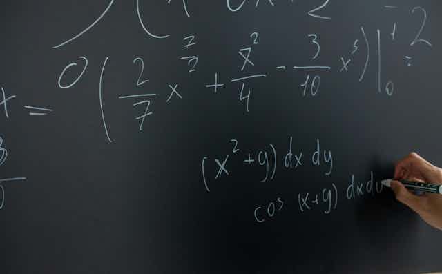 A hand writes equations on a board. 